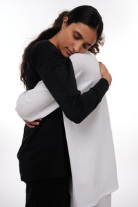 Two women embrace in black and white longsleeve shirts showing solidarity and compassion